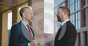 Two businessmen talking and shaking hands outside office