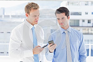 Two businessmen talking to each other and texting