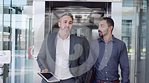 Two businessmen talking while walking out of an elevator