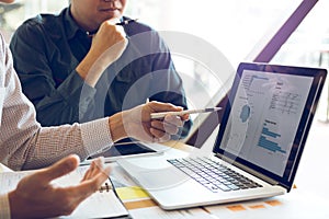 Two businessmen are together analyzing the financial data graph and pointing to the laptop computer screen