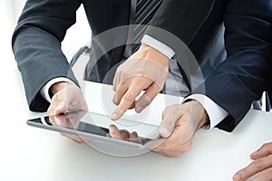 Two businessmen using tablet computer with one hand touching screen