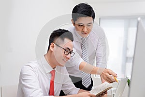 Two businessmen working together with computer at office desk, o