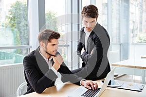 Two businessmen working and using laptop in office together