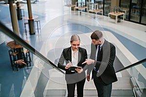 Two businesspeople looking at tablet while going up the escalator