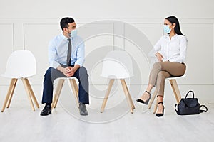 Two businesspeople wearing face mask while waiting for interview. Asian businessman and mixed race businesswoman keeping