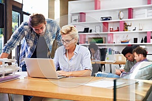 Two Businesspeople Working On Laptop In Busy Office