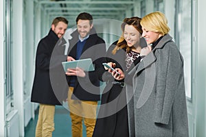 Two businesswoman looking smart phone in lobby with colleagues at background