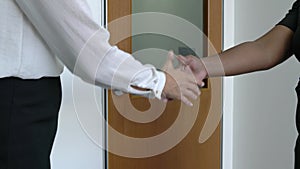 Two businesswoman shake each other`s hands at the office door. Closeup.