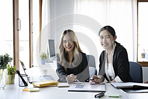 Two businesswoman sitting together in office and smiling to camera.