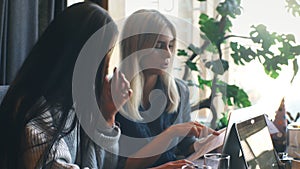 Two businesswomen are actively working on a laptop in a cafe and discussing the work