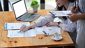 Two businesswomen colleagues analyzing financial statistics together at office desk.