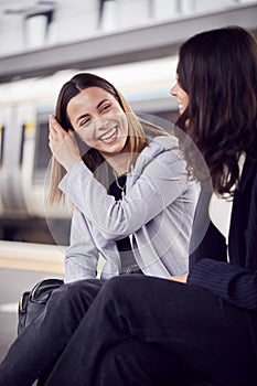 Two Businesswomen Commuting To Work Waiting For Train On Station Platform Talking Together