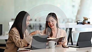 Two businesswomen employees colleagues using computer tablet and discussing working together. in office.