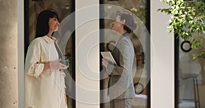 Two businesswomen lead friendly conversation standing in office hallway