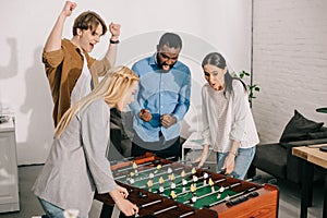 two businesswomen playing table football and male colleagues cheering up them