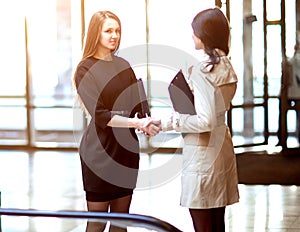 Two businesswomen shaking hands in the office lobby.