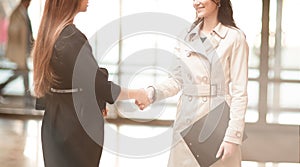 Two businesswomen shaking hands in the office lobby.