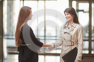 Two businesswomen shaking hands in the office lobby.