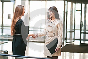 Two businesswomen shaking hands in the office lobby.