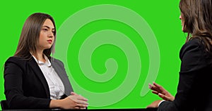 Two businesswomen sitting at a desk having an uninteresting interview, isolated on green background