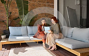 Two busy happy business women talking using tab working sitting in office.