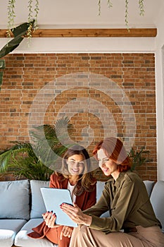 Two busy happy business women using tablet working sitting in office. Vertical.