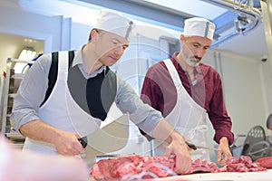Two butchers preparing meat in shop
