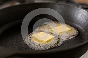 Two butter pats melting on a black cast iron frying pan.