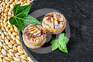 Two cake biscuits with white cream, banana slices and chocolate, on a slate dish on the background of a wicker table mat