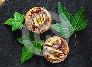 Two cake biscuits with white cream, banana slices and chocolate, on a slate dish on a black background