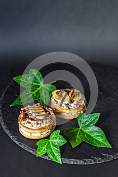 Two cake biscuits with white mascarpone cream, banana slices and chocolate, sprinkled with chocolate kerob powder on a slate dish