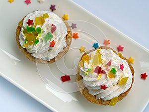 Two cakes are decorated with whipped cream, marmalade and pastry stars. Background with dessert