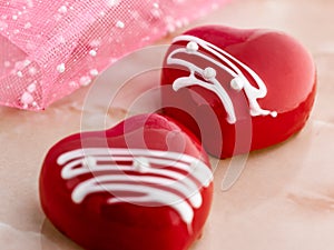 two cakes in the form of glazed red hearts on a pink marble table, close-up