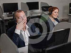 Two call center employees. A bored man and a friendly woman talking on a headset to clients.