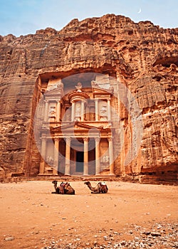 Two camels, saddles ready for tourists, sitting in front of Al-Khazneh Treasury temple - main attraction in Lost city of