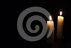 Two candles on black background. Lighting candles in darkness. Yellow wax candle with warm flame. In memoriam banner