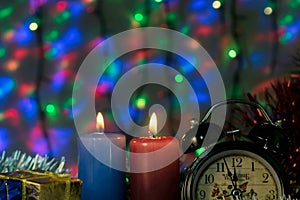 Two candles with clock and Christmas gifts with multi-colored lights on background