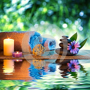 Two candles and towels black stones and purple daisy on water