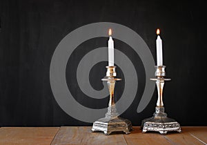 Two candlesticks with burning candels over wooden table and blackboard background