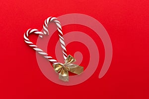 Two candy canes with bow making a heart on a red background.