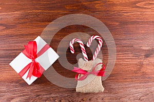 two candy canes with white gift box red ribbinon bow on dark wooden board