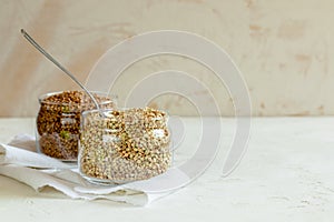 Two cans of buckwheat and spoon on white table with copy space.