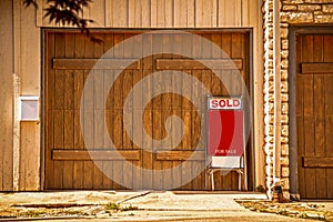 Two car garage with rustic wooden doors with for sale sign saying sold propped up against it - Copy Space