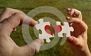 Two cardboard puzzles with a painted red heart are held in the hands