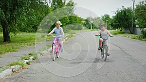 Two carefree children - a girl and a boy ride bicycles on the street. Steadicam shot