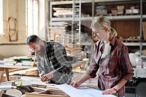 Two carpenters man and woman looking at blueprints indoors in carpentery workshop.