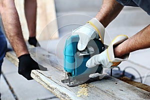 Two carpenters in working process in the carpentry workshop. Carpenter using fretsaw for cutting wooden boards. Construction