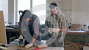 Two carpenters working with wooden planck and electric planer in workshop.