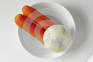 Two Carrots and one onion without peel on white plate. Top view fresh vegetable ingredients set for making vegan soup or