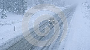 Two cars navigate along an icy road leading through forest caught in a blizzard.